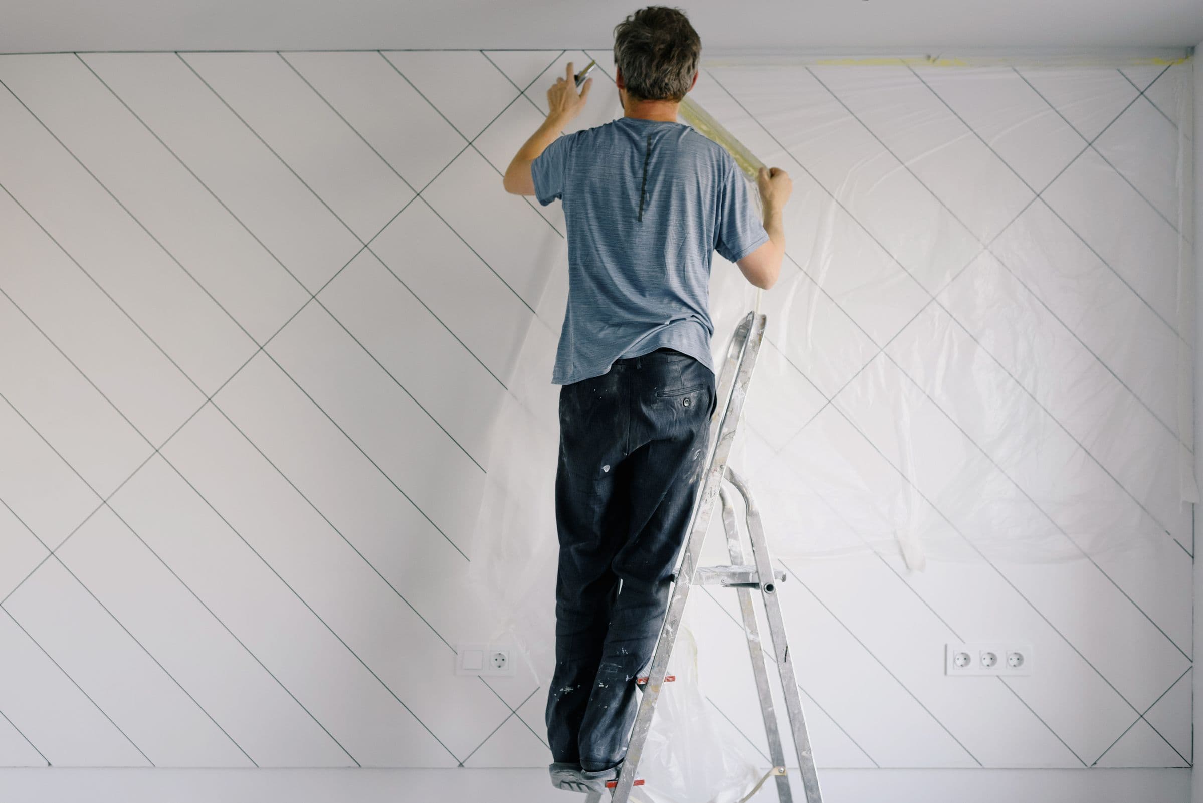 A painter carefully taping and finishing a wall inside a bright, modern room